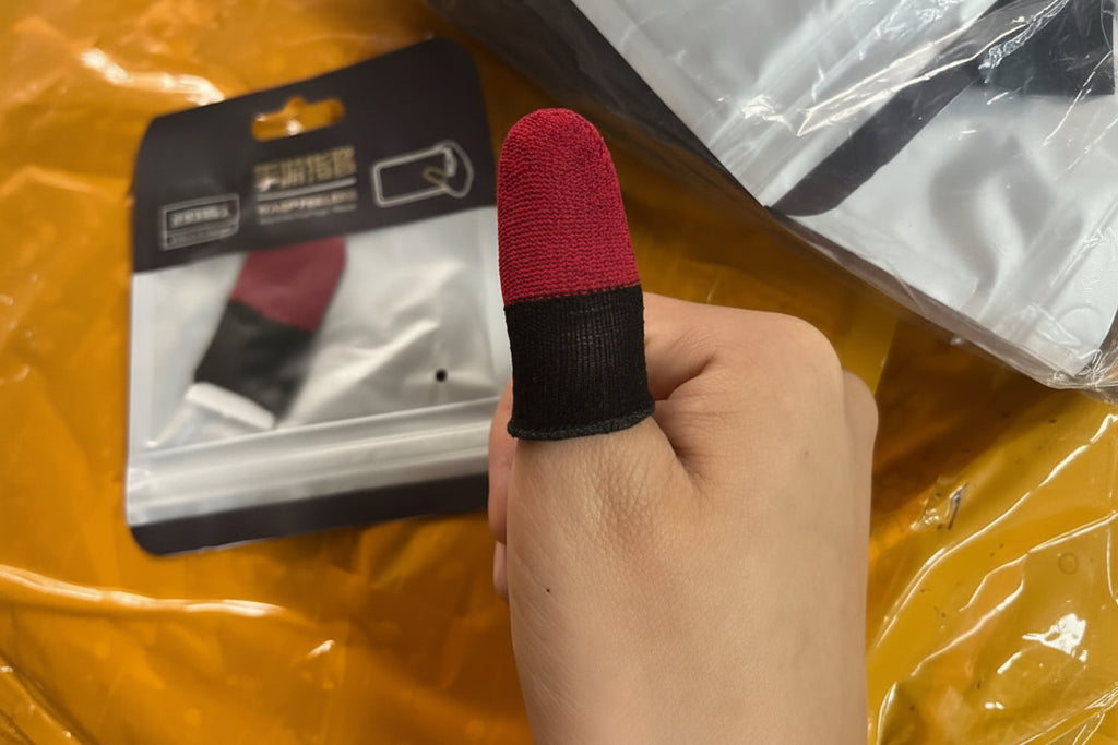 Hand holding a red and black finger sleeve with packaging in the background.