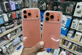 Two rose gold phone cases held in front of a store shelf with phone accessories.